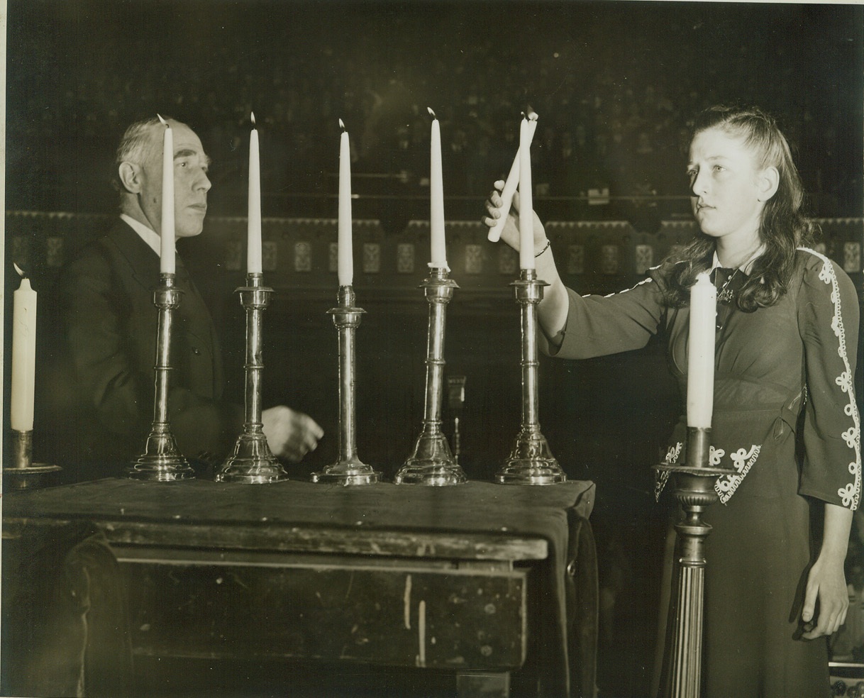 FOR HITLER’S YOUNGEST VICTIMS, 2/22/1943. NEW YORK CITY – Janine Putter, refugee child from France, lights one of the memorial candles at a Solemn Assembly of Prayer and Protest held at the Mecca Temple today by three thousand Jewish children from 518 religious schools in greater New York. The assembly was held for the children in Nazi-occupied countries. Credit: ACME;