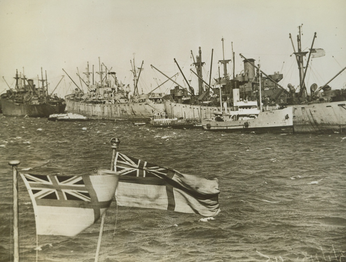 Liberty Ships Supply North African Forces, 2/13/1943. North Africa—A group of American “Liberty Ships” are pictured unloading at a North African port. In the foreground are the flags of two British destroyers. Credit: ACME.;