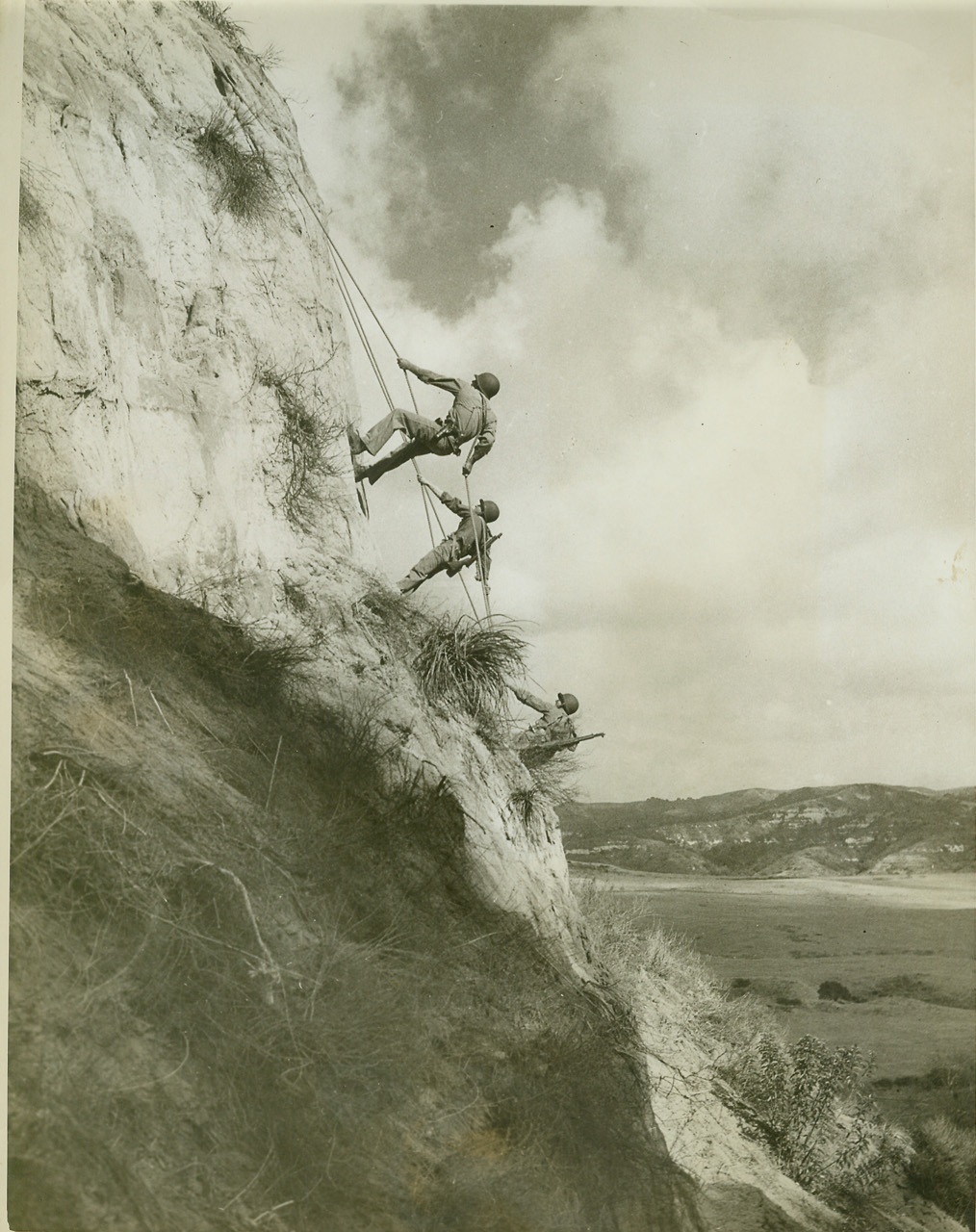 Marine Battle Tricks, 2/26/1943. Camp Pendleton, Calif.—Marine raiders scale a mountainside at Camp Pendleton where they are being taught savage methods for quick, quiet annihilation of the enemy. A battalion under the command of Lt. Col. James Roosevelt is now undergoing a tough course of instruction including mountain climbing, cable sliding for descending mountainsides at top-notch speed, construction of barriers out of natural material, and other rigorous maneuvers. Credit: U.S. Marine Corps photo, ACME.;