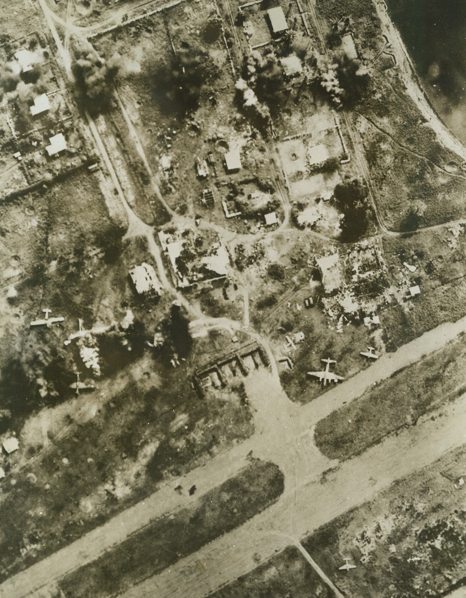 “DANGER! JAP-SMASHERS AT WORK!”, 3/8/1943. Japanese planes and installations on the airport at Lae, New Guinea, are shown being blasted to rubble in their photo taken from one of the squadron of raiding U.S. Army Air Force bombers, during a recent attack on the Nip base. In center, (photo above), can be seen roofless, burned out shells of buildings, while at lower left, American bombs make junk out of a group of Jap planes in the dispersal area. Other bomb bursts are marked by black smoke at top of photo.  Credit: U.S. ARMY FORCES PHOTO FROM ACME.;