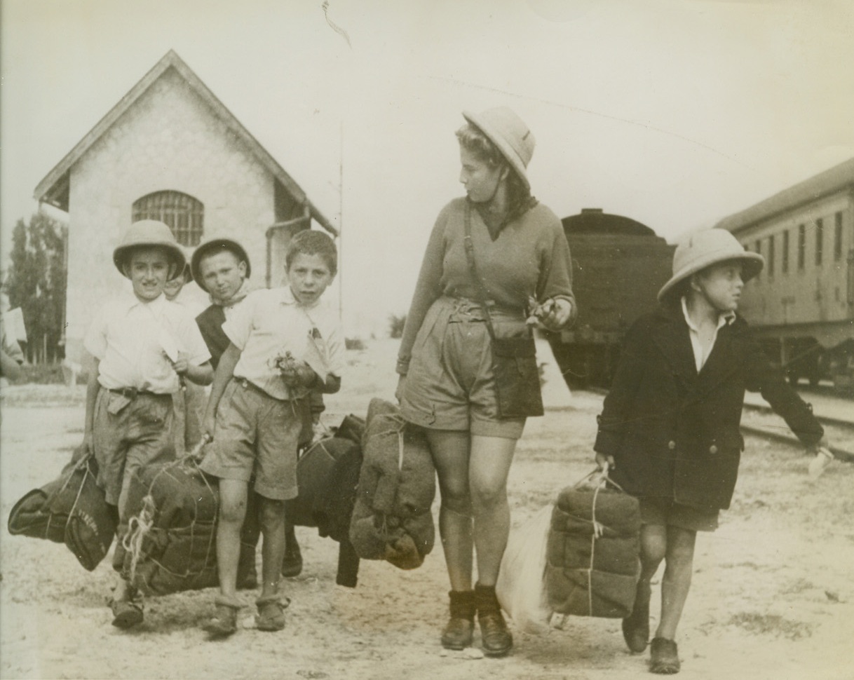 Safe At Least, 3/15/1943. Palestine – Toting their belongings, a group of young Polish refugees arrive safely in Palestine with one of the 50 children’s nurses who accompanied the youngsters.  They came from their homeland via Teheran.  Their education and maintenance in their new home will be financed by American funds. Credit line (ACME);