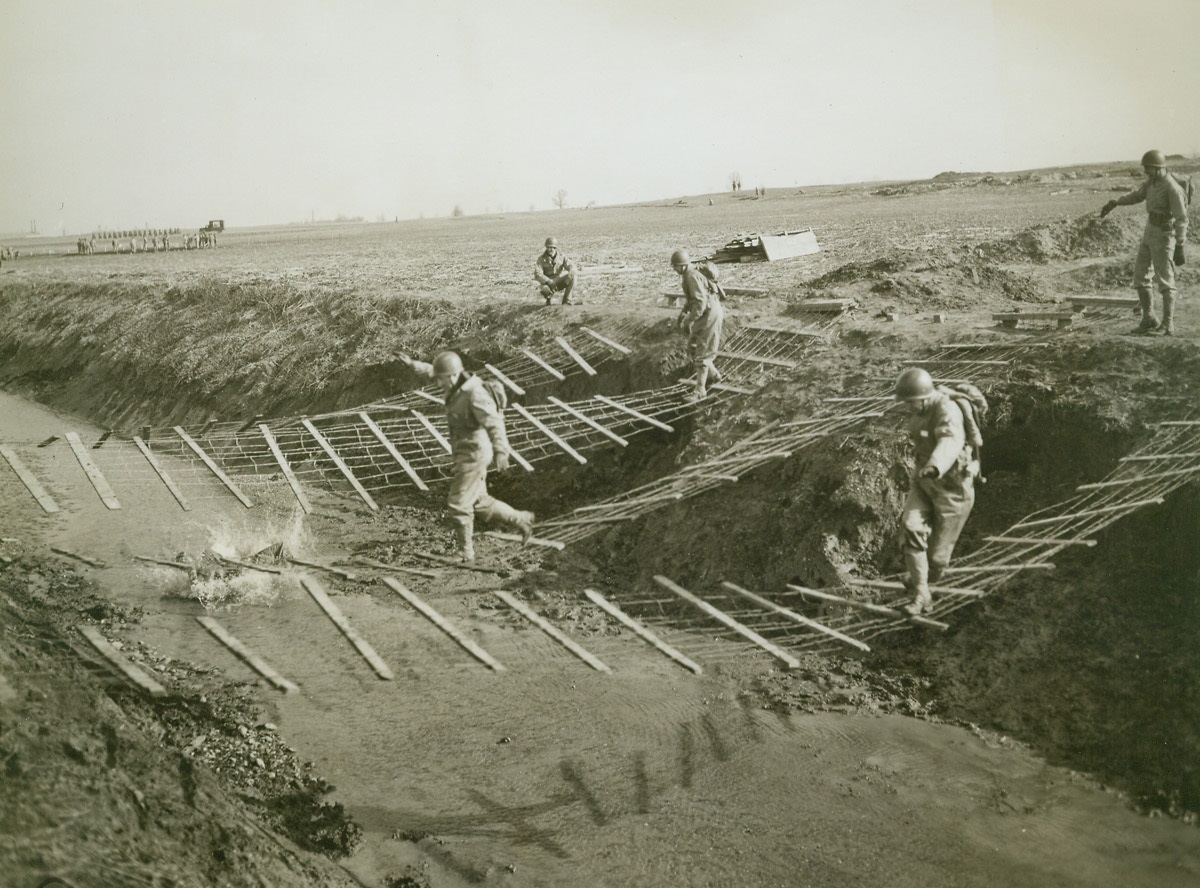 From Labor Leader to Tough Commando, 3/23/1943. Camp Atterbury, Indiana -- A trio of labor leaders swing-and-sway their way across wire bridges, where fence logs woven into the wire at two-foot intervals offer precarious footing. It’s part of the obstacle course that had United Automobile Workers, CIO, grunting and groaning during the first day of a three-day stretch in the army at Camp Atterbury. Credit: ACME;