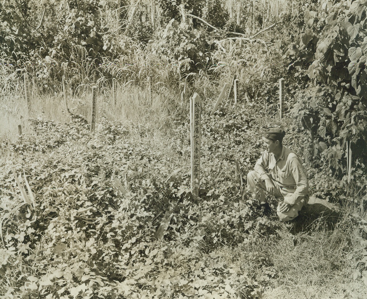 HERE LIES, 5/20/1943. NEW GUINEA—Deep in the heart of New Guinea’s Sananada Jungle, slender tombstones jut out of the foliage to mark the resting place of Japs who fell in conflict with Allied forces. Tom Yarbrough, a War Correspondent, reads the inscription that marks the grave of Rotsune Yamamoto of the Jap Navy. Credit: ACME;