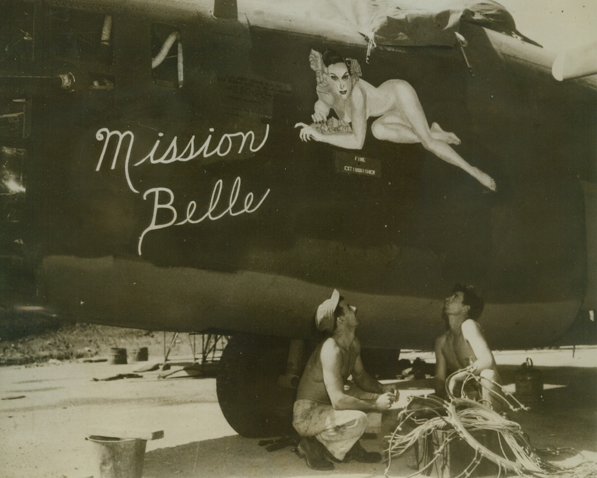 South Pacific Beauty, 6/14/1943. Southwest Pacific – Pfc Stanley Seaman, New Britain, Conn. (left) and Corp. Dean Thirkill, Los Angeles, Calif., are doing a repair job on the ignition system on one of the bombers that is flown daily over Jap bases in the Southwest Pacific area.  But the boys pause in their work to admire the provocative picture painted on the side of the plane.  Note sign, “fire extinguisher,” on side under the decoration. Credit line –WP- (ACME;