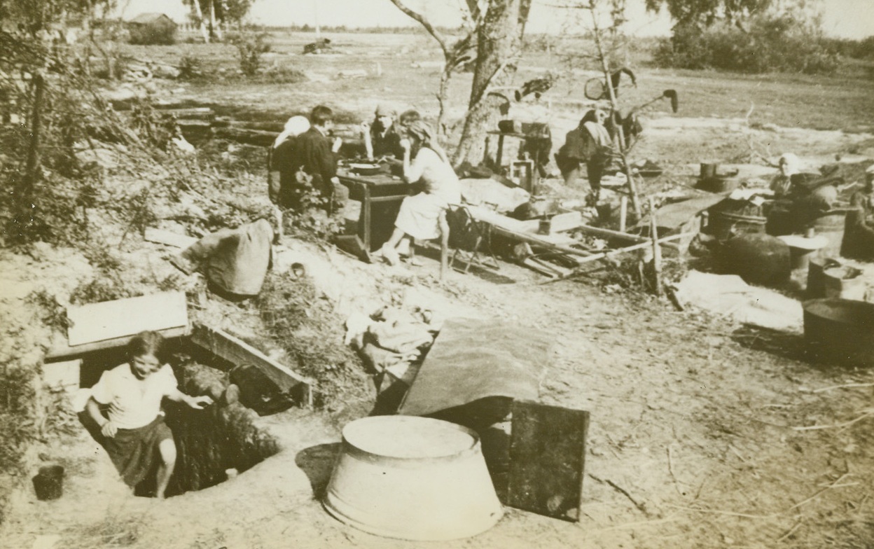 Picnic of Revenge, 1/4/1943. Kalinin Region, Russia—Soviet women and children live a communal life on the blasted battleground where their homes once stood in a village in the Zurtsov area of the Kalinin Region. Russian troops have driven out the Nazis, but the wreckage of war remains where families live in German dugouts and swear revenge. Credit: ACME.;