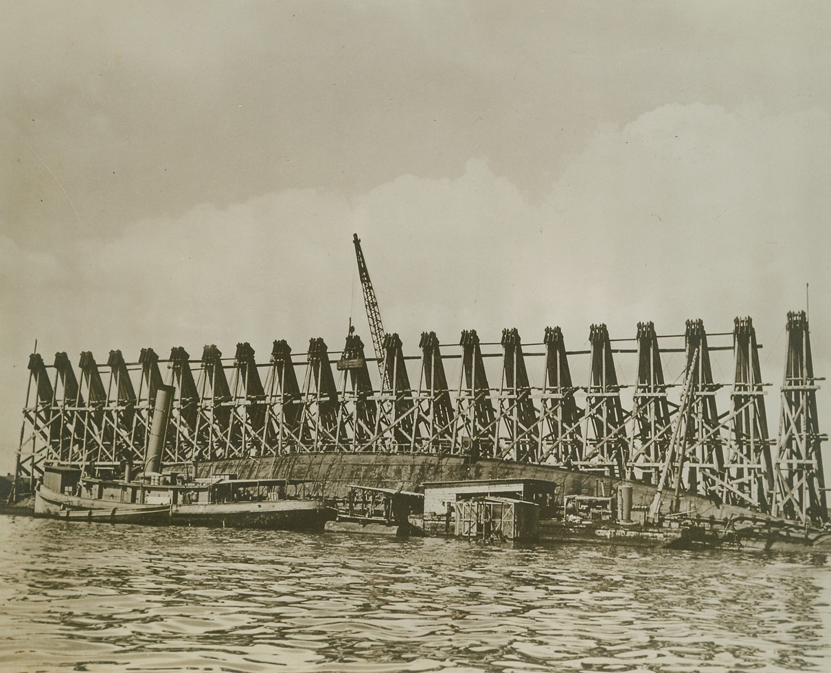 Raising the Battleship Oklahoma, 9/21/1943. This photo, just released by the U.S. Navy, shows the battleship U.S.S. Oklahoma being raised from the bottom of Pearl Harbor, where the warship was sunk during the Jap attack. Giant timber frames erected along the hull have cables running over them and to winches ashore, which slowly draw the vessel upright. Credit: (U.S. Navy Photo from ACME);