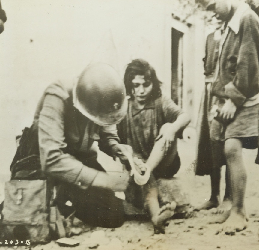 First Aid, 9/27/1943. ITALY – Lt. William E. King, chaplain, of Kansas City, Mo., administers first aid to a little Italian girl whose foot was cut by shrapnel. Photo by Acme photographer Charles Corte for War Picture Pool and flashed to U.S. by Signal Corps Radiotelephoto. Credit Line (ACME);