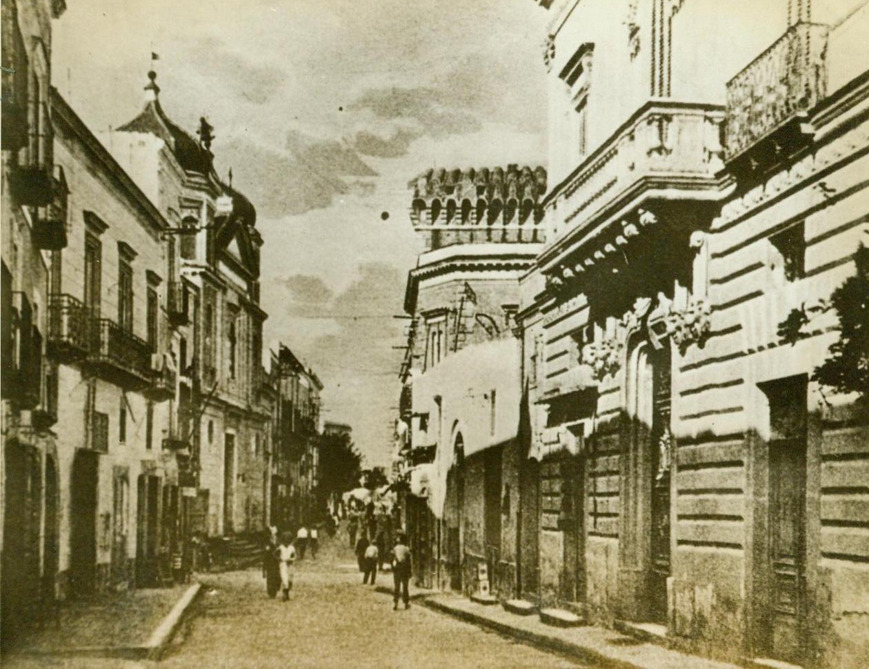 Scene On Captured Island, 9/18/1943. Pedestrians stroll through the central plaza of the city of Forio on the Italian island of Ischia, which fell to Allied Naval Forces on September 16th. One of two captured islands flanking Naples, Ischia’s fall brought the Allies virtually within sight of the great seaport. Ischia is only 7 miles from the Italian mainland. The other island, Procida, is 2 miles from the north peninsula skirting the bay of Naples. Credit Line (ACME). 9/18/43;