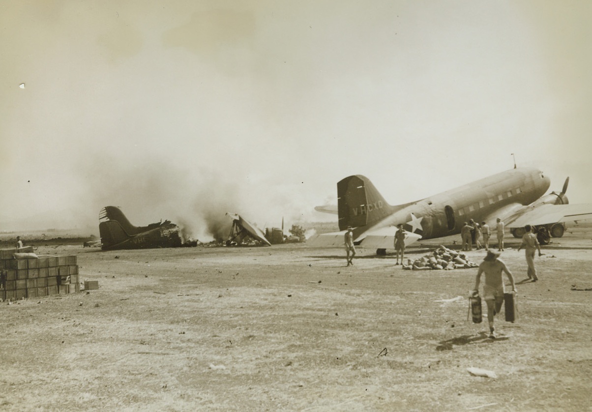 JAPS STRIKE FROM AIR, 9/14/1943. PORT MORESBY—A Jap bombing mission on the airport at Port Moresby, New Guinea, back in 1942 proved somewhat successful, jutting from the broken plane in background. While it burns unattended, ground men are fighting a fire inside the plane at right. The Australian soldier running toward the camera is carrying cans in which to get water. This picture has just been released by the War Department. Credit: ACME PHOTO BY FRANK PRIST, JR., CAMERAMAN FOR THE WAR POOL.;