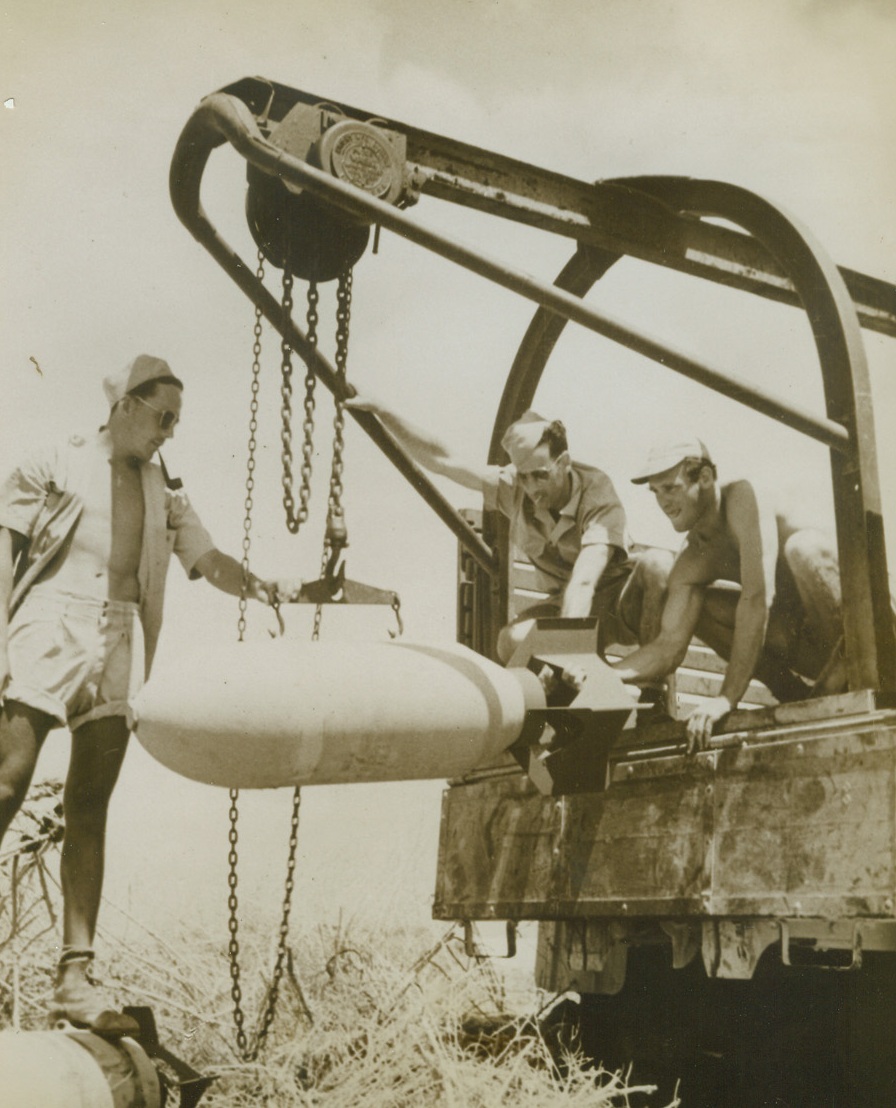 UP SHE GOES, 9/16/1943. IN THE CENTRAL PACIFIC—Three Air Force ordnance men load a 500-pound bomb into a truck at a Central Pacific base where personnel of the Seventh Army Air Foce are trained. Left to right: S/Sgt. Nicholas Karpinsky, Passaic, NJ; Pfc. Donald Arehart, Earlham, Ia.; and Sgt. Robert Cuinn, New York City. Credit: ACME.;