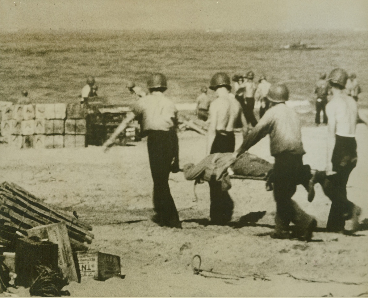 Return From Battle, 9/30/1943. Salerno – Returning from the battle of Salerno, this American fighting man travels across the beach to a waiting transport by stretcher.  The casualty was brought to a hospital by the same coast guard manned boat that brought supplies in background.  He was one of approximately 12,000 Yanks wounded, killed or missing in action during July 10th and Sept. 15th. Credit line (U.S. Coast Guard photo from ACME);