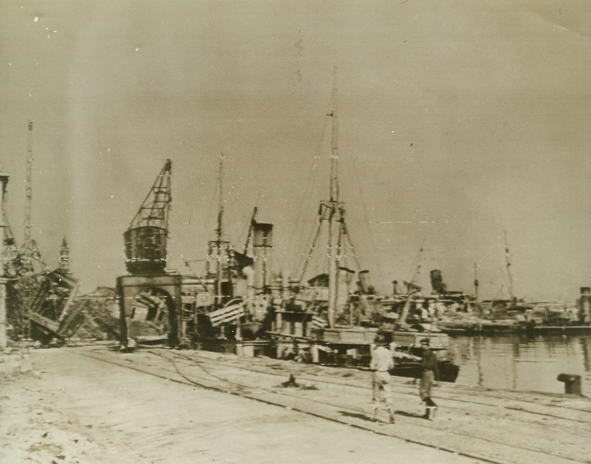 Wrecked Naples, 10/3/1943. NAPLES, ITALY—Accompanied by a Naples policeman, an American soldier sets out to examine ship wreckage in the Italian city’s once-proud and beautiful harbor. Fleeing Germans destroyed as many of the city’s harbor installations and ships docked where as they could, before they fled. Credit: Photo by Charles Corte, ACME PHOTOGRAPHER FOR WAR POOL, ACME.;