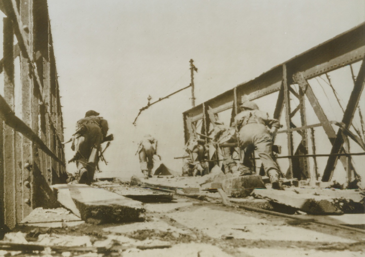 BRITISH WAVE CROSS THE VOLTURNO, 10/26/1943.CANCELLO, ITALY—Bending low and with their guns held ready for instant use, British infantrymen dash across the blasted railway bridge over the Volturno River to enter Cancello, in this photo flashed to New York by radio today. It was announced today that the Allied 5th and British 8th armies had advanced up to six miles and had taken 10 more towns. Credit: British Army via OWI Radiophoto from Acme;