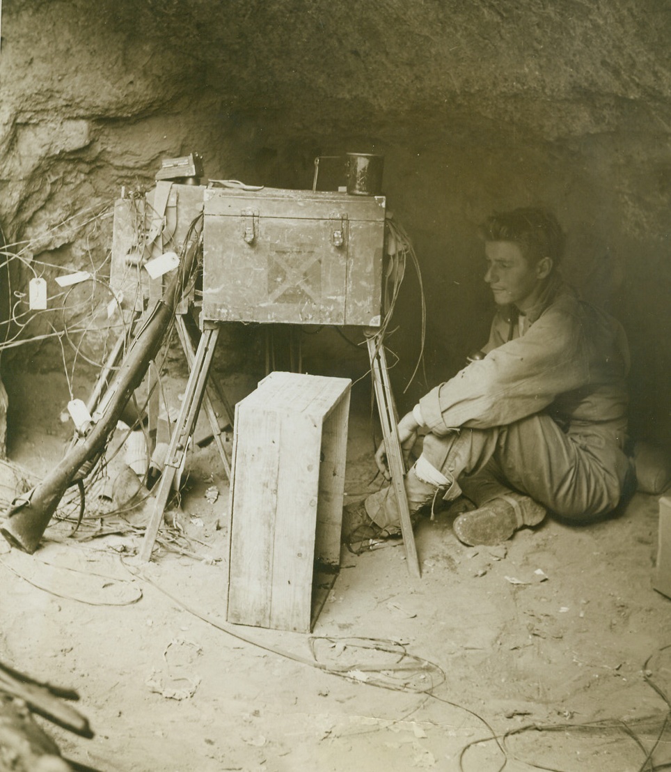 NOISY SWITCHBOARD, 10/24/1943. ITALY—Pvt. Thomas Krezan, of Slickville, Pa., operates as middleman between the Allied front line units and headquarters, during the 5th Army fight to span the Volturno. With his telephone switchboard, he is dug in only 800 yards from the river. Credit: Acme photo by Bert Brandt, War Pool Photographer;