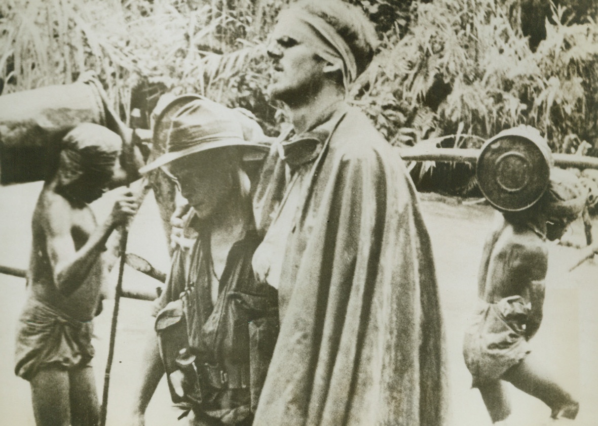 COMRADES AT ARMS, 10/21/1943. NEW GUINEA—A wounded Allied soldier grasps the shoulder of Sgt. Gordon Ayres, of Shepparton, Victoria, who helps him across a creek to a dressing station. This action, during the advance on Salamaua, New Guinea, takes place in a drenching rainstorm. Credit: Acme;