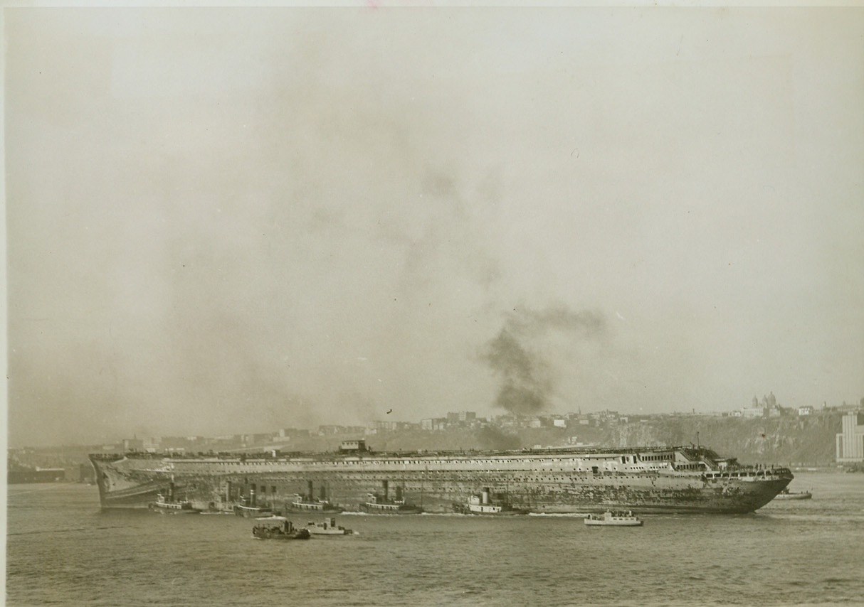 GHOST OF FORMER SELF, 11/3/1943. NEW YORK – Her superstructure removed, the U.S.S. Lafayette, formerly the French Luxury Liner Normandie, is towed down the Hudson River, Nov. 3, en route to drydock at an undisclosed destination. It is the first time the ship left her pier in four years. Time can only tell the next chapter in the life of the great liner. Credit: OWI Radiophoto from ACME;