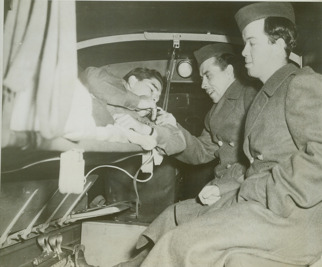 FIRST AMERICAN WOUNDED REPATRIATED FROM GERMANY, 11/2/1943. WASHINGTON, D.C. – Fourteen wounded American soldiers, the first to be repatriated from Germany under an agreement for the exchange of sick and wounded prisoners, arrived by plane at the National Airport and were immediately transferred to Walter Reed Hospital. Staff Sgt. August E. Tornow, of Springfield, Ore., (center) lights a cigarette for Corporal Rodney M. Graham, (left) of Atoka, Okla., as Tech Sgt. John H. Gardner, Yoakum, Texas, (right) looks on. Credit: U.S. Army photo via OWI Radiophoto from ACME;