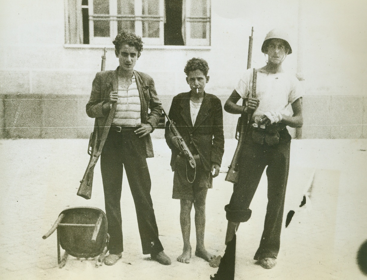 NAPLES FIGHTS NAZI TERRORISM, 11/2/1943. This series of photos, just released in the United States, tells the graphic story of the German rape and pillage of Naples, how they killed Neapolitans just because they were Italians, and how Nazi demolition squads razed buildings and beautiful landmarks of no military value—but to create another blackened and twisted monument to German terrorism and vengeance. But Naples fought back and many young Italians—some only 14 years old—brought out firearms that they had kept hidden and, for three days before the Allies captured the city, kept up guerilla battles against the Germans. These young lads, who were members of an anti-Fascist organization led by one Antonio Tarsia, killed as many as 30 Germans each day by ambushing them and sniping from rooftops. The fighting, however, was one-sided in the face of the superior numbers of the Germans. About 2,000 citizens of Naples were shot down in the streets or in their homes just because they happened to be Italians.  NEW YORK BUREAU Three youthful snipers, who carry their weapons in an easy and experienced manner, are ready to set out on a Nazi-slaying hunt. The lad at right, wear a combat helmet and has a bandaged left hand. Credit: Acm;