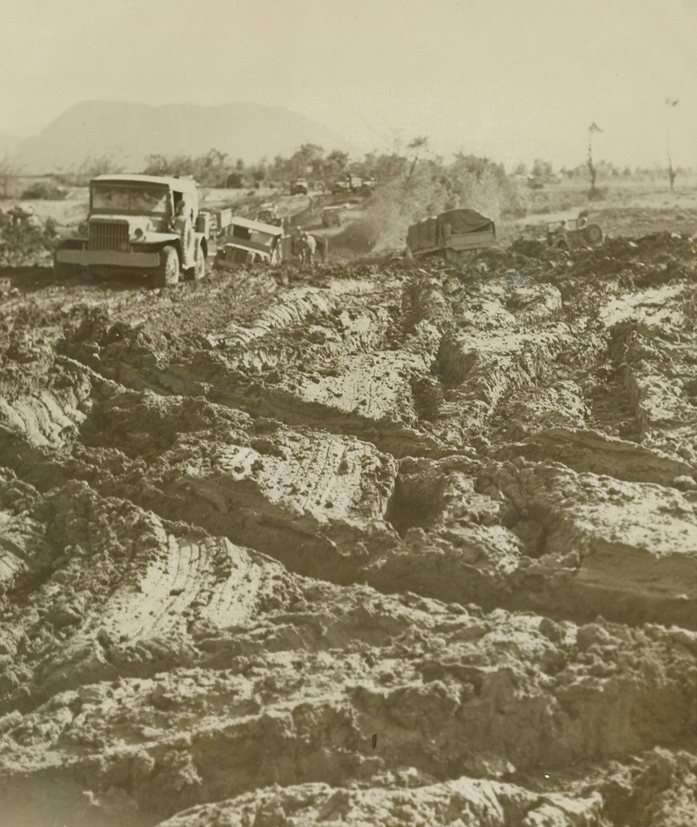 BLITZ BOTTLENECK, 11/23/1943. WITH THE 5TH ARMY IN ITALY—This quagmire along the front in Italy, passes for a temporary road for vehicles bypassing a bridge blasted by the Germans in their retreat to Cassino. In the background, an American Jeep and truck seem to be hopelessly mired in the sticky, mud. Credit Line (ACME Photo by Bert Brandt for the War Picture Pool);