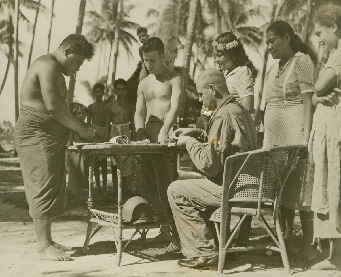 Pay-off Day, 11/26/1943. At a South Pacific Base – Lucky Marines at this South Pacific base don’t have any wash-day blues.  Women of the island take care of the laundry problem for a mere $2.50 per month, per Marine.  And here’s the payoff, Marine Gunner O.A. Powell settles his bill with 230 pound Noa (left) acting as an interpreter and Platoon Sgt. James G. Hayes (seated) of Donalsville, GA., supervising. Credit (U.S. Marine Corps photo from ACME);