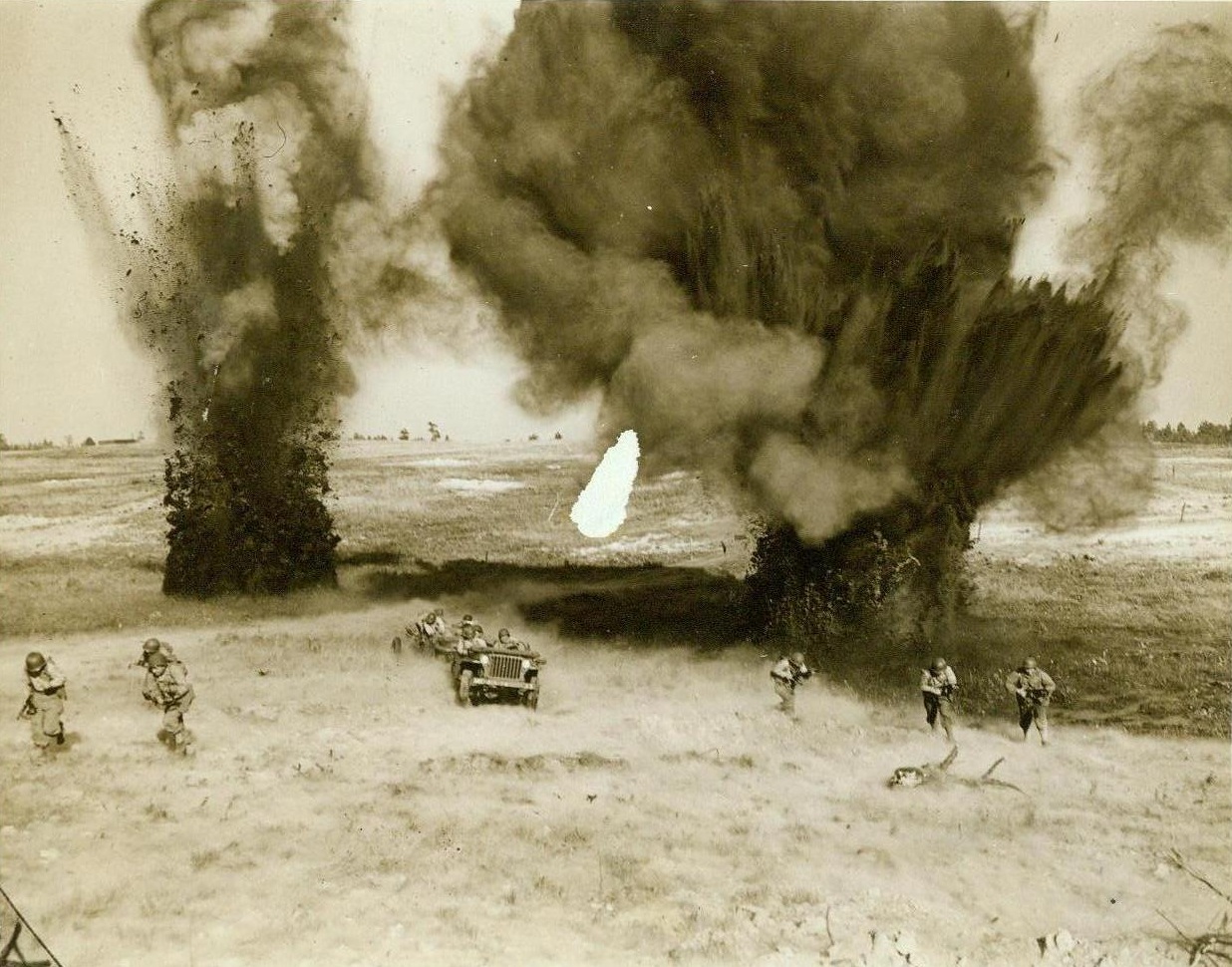 Uncomfortably realistic, 11/23/1943. CAMP MACKALL, N.C. – Men from the 465th Glider Field Artillery Battalion advance on either side of jeeps as simulated shell bursts help them to pick up their heels at Camp Mackall, N.C. They charge across a field which contains several pill-boxes and other “enemy” defenses, training for the kind of opposition which other American airborne troops have already met up with overseas. CREDIT LINE (ACME) 11/23/43;