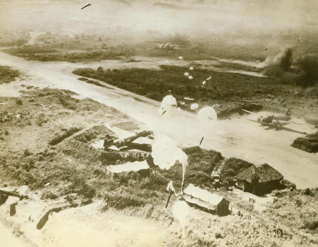 Yanks Blast 200 Jap Planes At Rabaul, 11/4/1943. This unusual photo, taken from a plane of the U.S. 5th Air Force, which was flying almost at rooftop level, shows a string of parachute bombs (from lower center to top center of photo), as they dropped on a section of the dispersal area of Vunakanau Airfield at Rabaul, New Britain, during a raid last Oct. 12. More than 200 Nip  planes were destroyed or damaged in the raid, as well as ships and installations. Note Jap bombers in their revetments, while a zero fighter, (lower left) is cracked up in a ditch. Last Tuesday, Yank airmen struck at Rabaul again, damaging or destroying 26 ships and 108 planes. (U.S. Army Air Forces Photo From ACME);