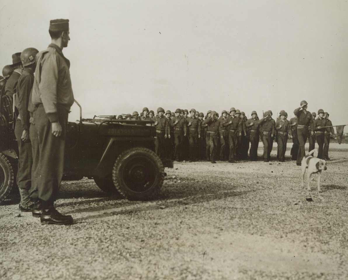 MASCOT PARADES, TOO, 12/15/1943. SICILY—Touching their battle-helmets as they march in review before their distinguished visitor, President Roosevelt, these veterans of the Sicilian campaign are led by their unconcerned mascot, who ambles along with…FDR a second glance. In left, fore-…Lt. Gen. Mark W. Clark.;