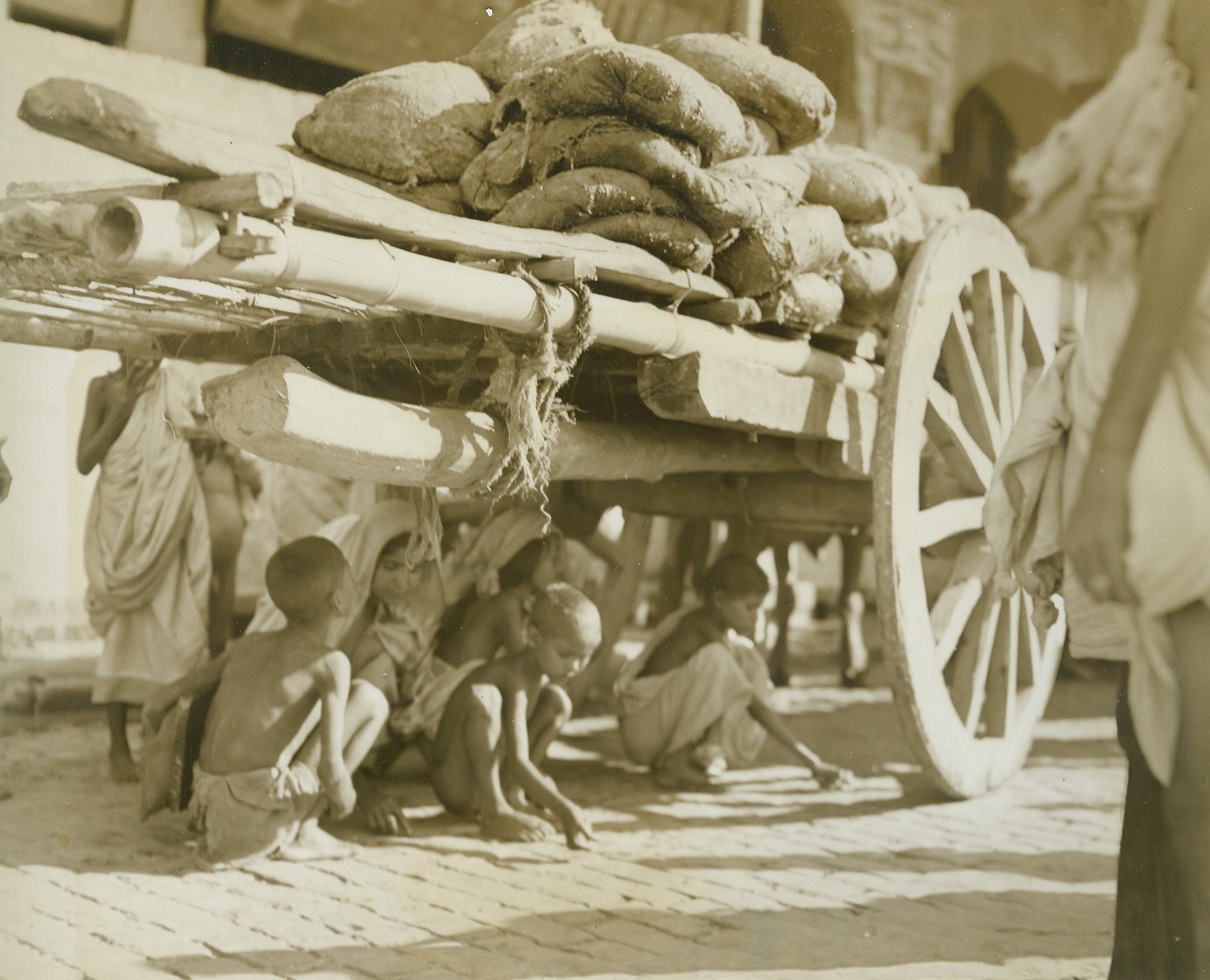 Famine in India, 12/17/1943. By last week, an estimated 1,000,000 persons had died of starvation in India and, although the British government reportedly has the situation under control that number will undoubtedly be raised before the final, tragic count is taken.  Just released, these startling pictures were taken in Calcutta at the peak of India’s famine in late October when a homeless army of 100,000 roamed the city, dying in the streets. New York Bureau It doesn’t take long for word to get around that grain is spilling from these sacks on a wagon parked in Calcutta.  Children, who dare not rip open the bags, grub in the dirt for kernels that sift down. Credit line (ACME);