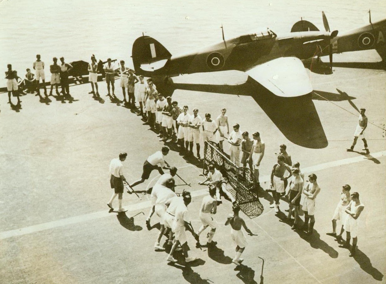 Mediterranean Sea Hockey Match, 10/23/1942. Somewhere in the Mediterranean – Hurricanes stand ready for action in the rear, while a hockey game is in full progress forward, on the deck of a British Aircraft Carrier somewhere in the Mediterranean. An interested audience watches the flight deck match, and aerial and sea warfare seems far away, instead of just around the next cloud or wave 10/23/42 Credit Line (ACME);