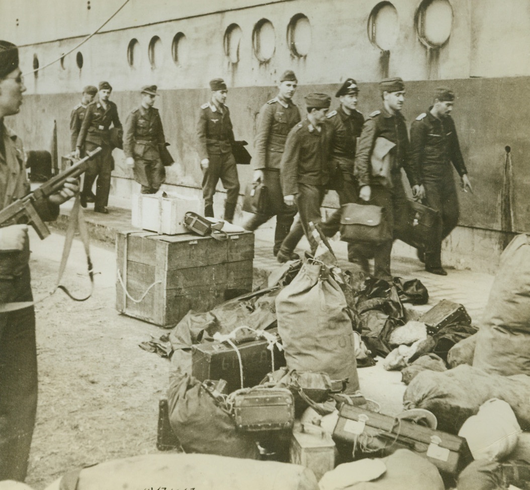 Rounding Up the Enemy, 12/19/1942. Algiers, Algeria—Under the watchful eye of an American soldier with a Tommy gun, German prisoners march onto a boat which will take them to a prison camp. American and British troops, soon after landing in North Africa, rounded up all enemy personnel and evacuated them from the area, to the obvious delight of the natives. Latest reports from North Africa indicate that American flying forces continue to pound the Axis in Tunisia while ground patrol activity of the Allies increases. Passed by censor. Credit: ACME.;