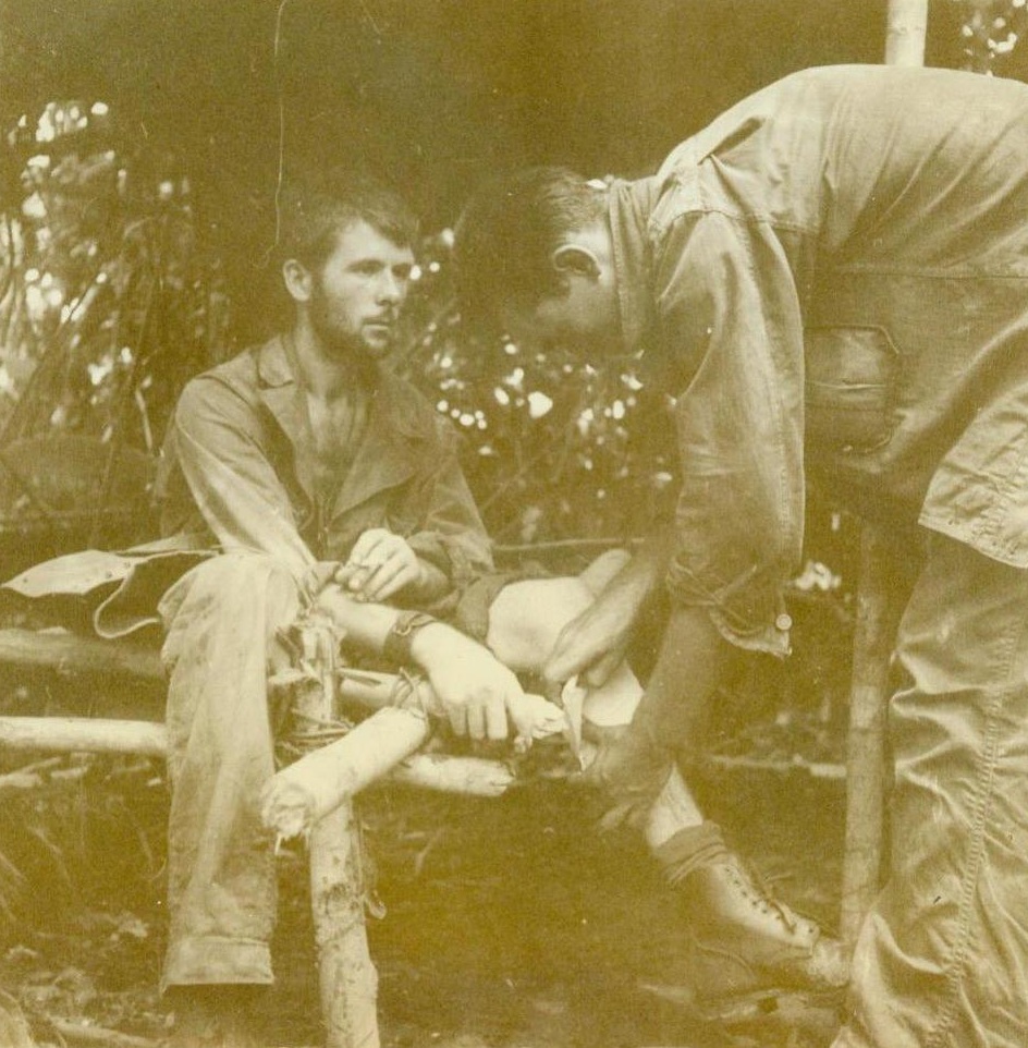 He Can Take it!, 12/15/1942. New Guinea – Described as a “wild man” by his buddies and credited with killing between thirty and forty Japs, as his unit crossed New Guinea on their way to strike at the Nips in the Buna-Gona area, Pfc. Orin Sutton, (left), of Charlevoix, Mich., couldn’t be worried by a mere Jap machinegun bullet. He was back in action in a few days. Pfc. Allie Poole, of Petersburg, Mich., is shown, (photo above), bandaging the wounded leg. This photo has just been released in Washington. CREDIT LINE (ACME) 12-15-42;