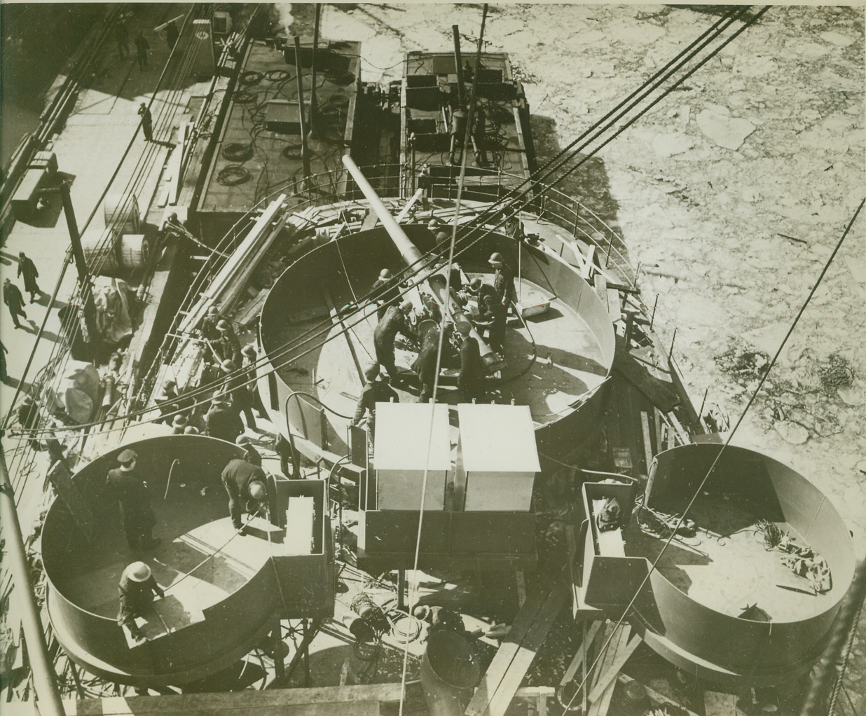 Navy Speeds Army of Merchantmen, 4/9/1942. Workers, shown as they make final mechanical adjustments on a heavy gun, (center), which rests in its steel-protected emplacement aboard a merchantman, in a shipyard “somewhere in the United States.”  Credit: Official Navy photo from ACME.;