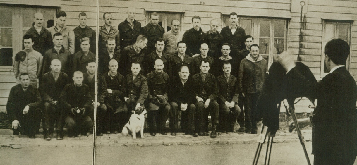 JAP PROUDLY PHOTOGRAPH THEIR WAR PRISONERS, 9/11/1942. SHANGHAI—In a caption accompanying this photograph in “Freedom,” Japanese propaganda magazine published in Shanghai, this scene is described as U.S. and British was prisoners being photographed by a professional Jap cameraman in Shanghai concentration camp. Purpose of the picture, like all those published in the magazine, is to show that the Japs don’t mistreat their prisoners. “The camp mascot was not forgotten,” the caption points out—no doubt one of those warm, human touches for which the perpetrators of Pearl Harbor are famous. Credit: ACME.;