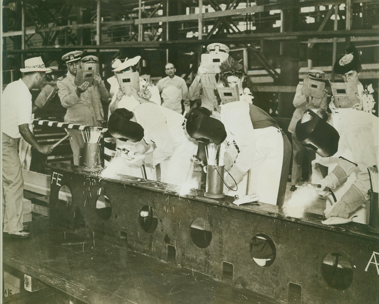 LABOR DAY KEEL LAYING AT CHARLESTON, 9/8/1942. CHARLESTON, S.C. – The first wartime Labor Day found workers at the Navy Yard here putting in a full day on the job and then attending the laying of keels for two landing ships. Striking arcs on one of the new keels are, L. to R., F.O. Tillman, Robert Kellahan, and Moses B. Rayes. Their proud wives stand behind them watching with aid of protective face shields. Credit: U.S. Navy photo via OWI Radiophoto from ACME;