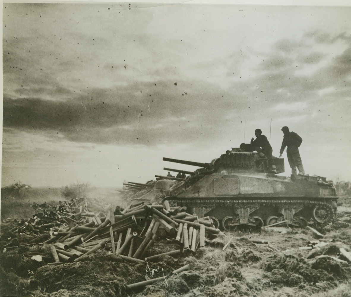 British Tank Battery Assails Germans, 11/26/1944. Germany – Standing behind the turrets for protection, crew members of twelve British tanks fire away at German positions on the road between Gangelt and Geilenkirchen in Germany. In front of the tanks are mounds of empty shells. Credit: (ACME) WP;