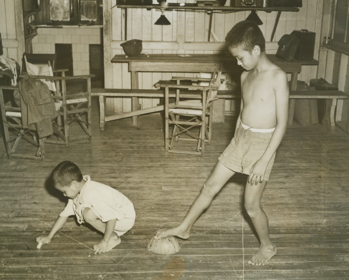 Four Hands Better Than Two, 11/18/1944. Tacloban, P.I. - - Carlos Benitez, 12, and Pablito Benitez, 8, give a demonstration of the Filipino method of polishing the floor.  Pablito applies the wax candle stick, then Carlos follows up with his two cocoa nut husks to polish.  If Carlos gets tired polishing with his hands he’s just as capable of continuing his work with his foot: Note the difference in polished and unpolished floor.Credit (ACME photo by Stanley Troutman, War Pool Correspondent);