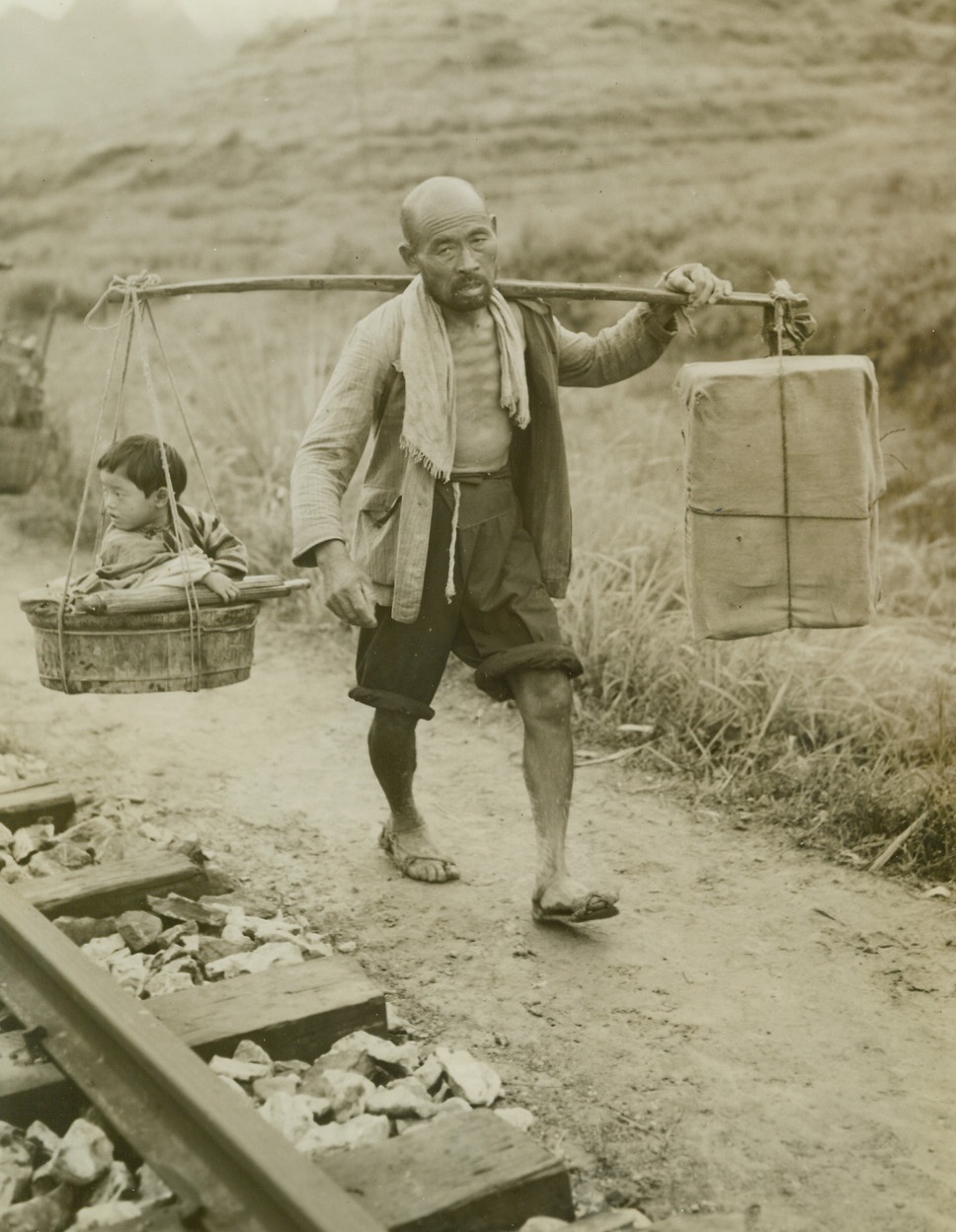 China’s Human Cargo, 11/10/1944. Eastern Front, China – Masses of humanity, united in one common purpose – flight for life—cram the railroads and highways leading from China’s Eastern front, as the instinct for self preservation sends them fleeing from Jap terror.  Simple peasants they are, familiar with only the ways of simple folk like themselves, but they know the atrocities of the Japs, rather than live under the yoke or the rising sun, they choose to suffer hardship, and even death, to evade them.  Trains leaving Liuchow are packed from the rails to the tops of the cars, and all available vehicles fill the highway as shown in this unusual and dramatic series of photos made by Frank Cancellare, ACME photographer for the War Picture Pool  On the heels of the evacuees follow constantly the fear of the dread typhus and cholera epidemic but still they go onward. New York Bureau Weary from lack of rest and nourishment, this father bows under the yoke on which he carries his young son in a basket.  He balances his burden with a box on the other end, which carries some of the family belongings.  Photo by ACME photographer, Frank Cancellare, for the War Picture Pool. Credit – WP – (ACME);