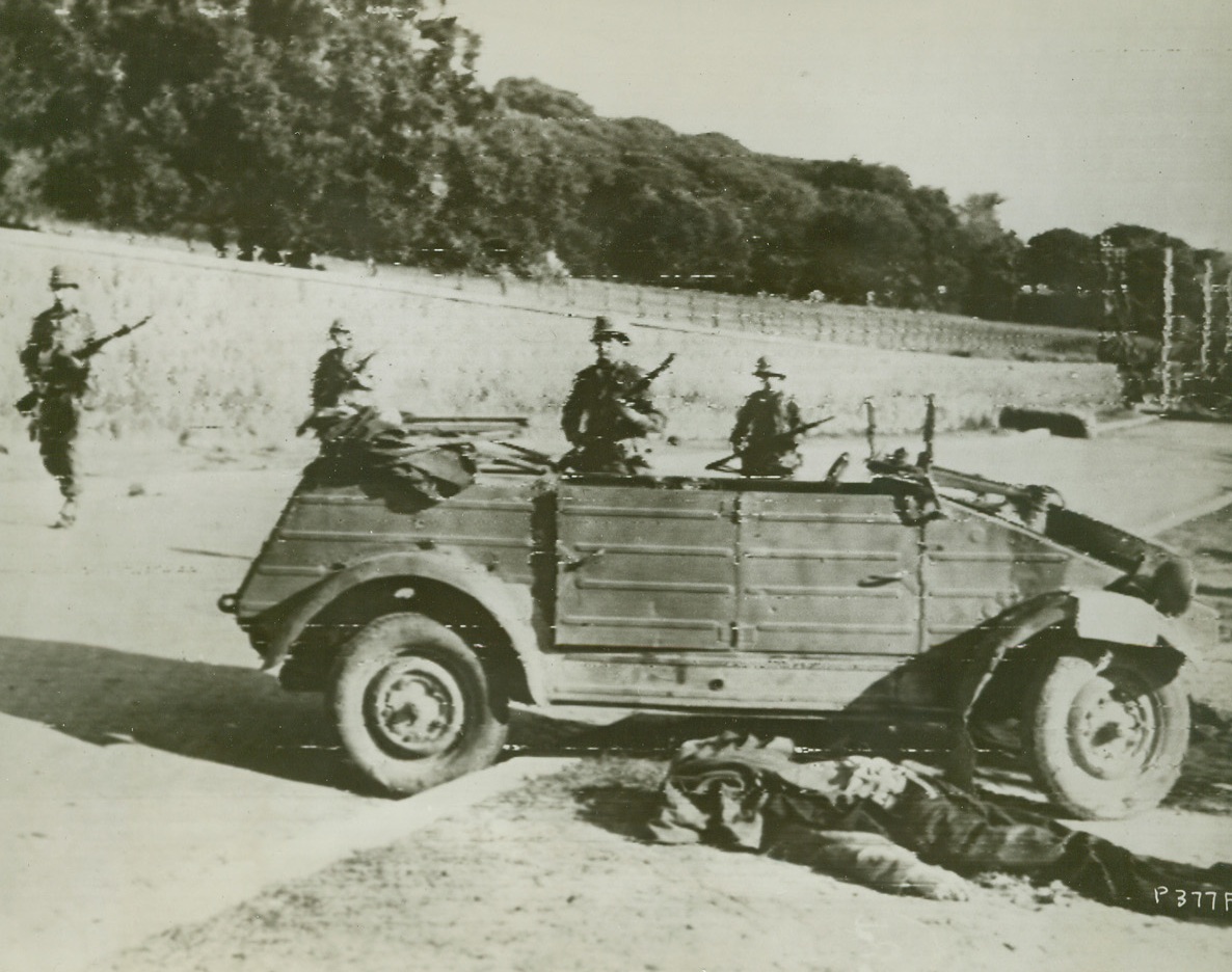 Yanks Advance Cautiously in Anzio, 1/27/1944. Anzio, Italy—Wary American soldiers, holding their guns ready for use in a split second, advance cautiously along a street in Anzio, after the Germans had been driven out by the invaders. A dead soldier lies before the German Jeep in the foreground. Credit: U.S. Signal Corps radiotelephoto-ACME.;