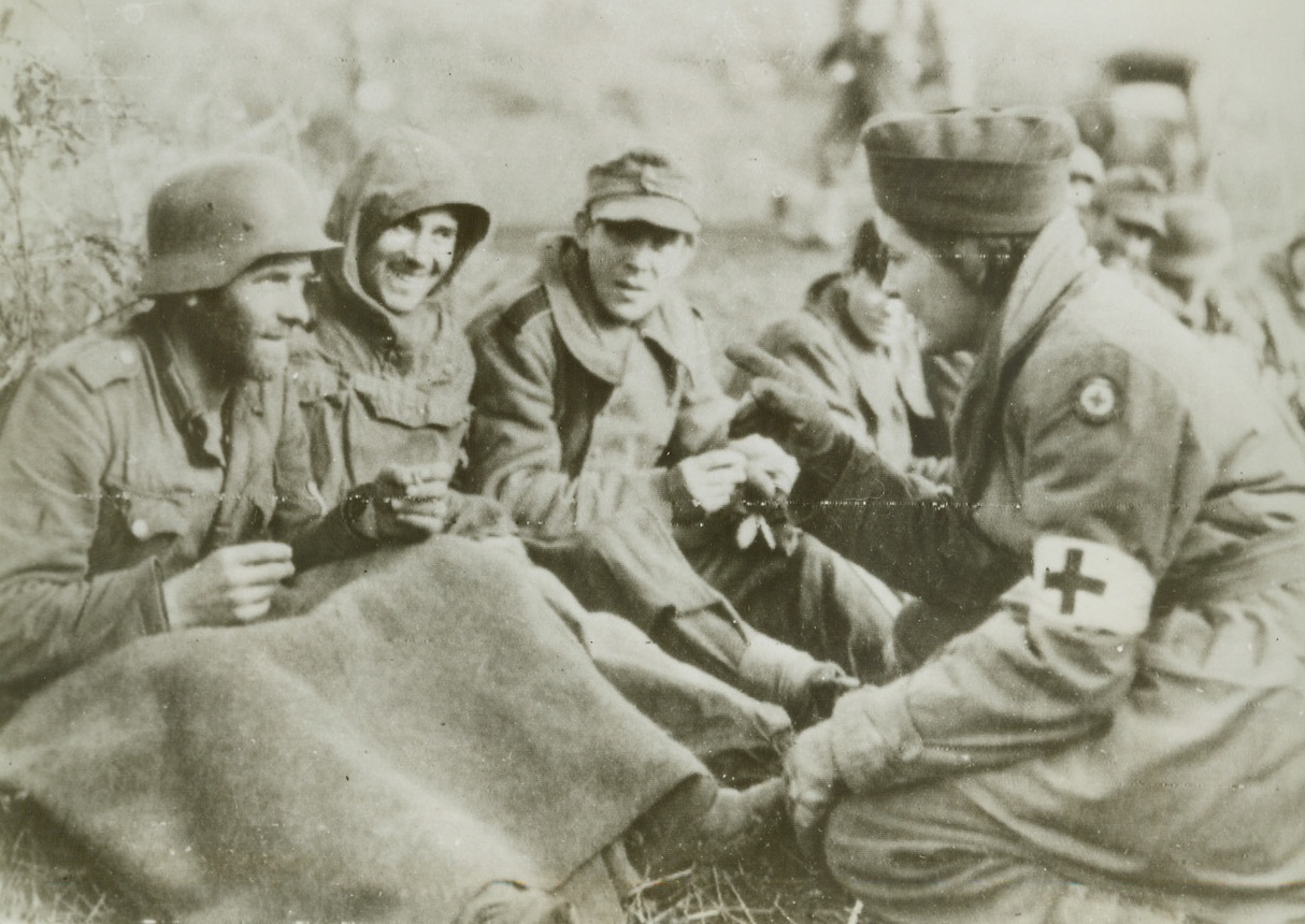 PRISONERS SMILE, 1/18/1944. SOMEWHERE IN ITALY—A French girl ambulance driver, serving with the Fifth Army in Italy, wins a smile from these captured German warriors taken by French troops. Forsaken by their comrades, the Nazis appreciate the kind treatment given them by Allied mercy workers. Photo radioed from Algiers today (Jan. 18th).Credit: Acme Radiophoto;