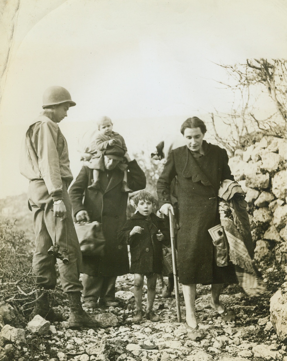 Return of the Natives, 1/1/1944. LAGONE, ITALY – Scene of many days of bitter fighting, the tiny mountain town of LaGone fell to warriors of Lt. Gen. Mark Clark’s Fifth Army, and the smoke of battle hardly cleared before hundreds of natives flocked down from the hills to return to their homes. The pathos of their tragic homecoming to the wrecked, blasted building is recorded in this series, made by Acme correspondent Bert Brandt for the War Picture Pool. Non-combatants all these men, women and children find that war is a very personal experience nevertheless: an experience that has left them with a deep, grim hatred for the Germans.New York BureauA tiny tot rides atop his father’s shoulders, and his mother walks with a cane as this family returns from the hills. At left is Lt. Harry McKinnon of Charlotte, N.C., who is in charge of a group of combat engineers.;