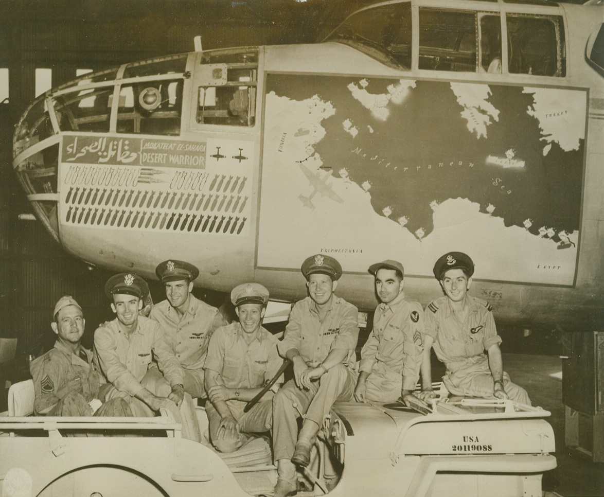 Next Mission—U.S.A., 1/10/1944. North African Theatre—The “Desert Warrior”, a well-decorated Mitchell B-25 bomber of the U.S. Army 9th Air Force, is shown just before it was taken by its crew to the United States after completing some of the most historic missions from the war from El Alamein to Sicily. The crew members seated on the Jeep are (left to right): Sgt. John R. Dawdy, of San Antonio, Tex.; Lt. Floyd R. Pond, Anadarko, Okla., navigator; Capt. Ralph M. Lower, Spokane, Wash., pilot; Lt. T.R. Tate; Lt. W.O. Seaman, Fresno, Calif; Sgt. J.B. Saragalo, Queens, N.Y.; and pilot officer A.A. Martin, British, of Columbia, Canada. The bombs painted on the cowling of the “Desert Warrior” represent the missions this ship performed. On the map are recorded the individual towns and battlefields bombed. Credit: U.S. Signal Corps photo from ACME.;