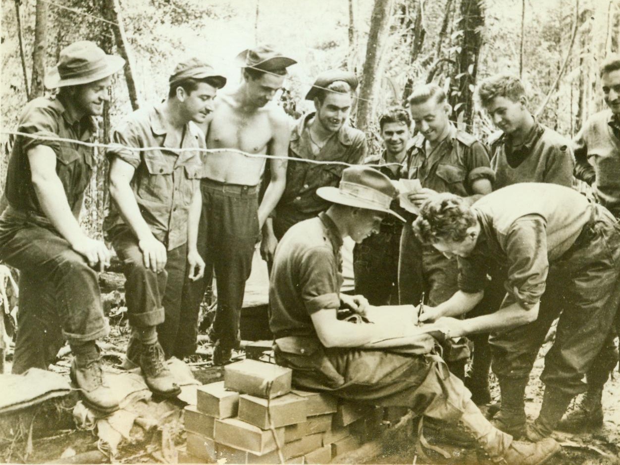 Nobody Denied Aussies Their Vote, 1/14/1944. NEW GUINEA - Neither the whims of Congressmen nor a complicated balloting system robbed Australian fighting men of their right to vote in their country's federal elections. Looking on as Cpl. A.E. Tierney of Wonthaggi, Victoria, signs the envelope in which his ballot is sealed, American troops wonder they'll be allowed to do the same when their countrymen go to the polls. Seated is Lt. Larry Drake of Draling, Victoria, the unit's electoral officer, who supervised the balloting only half a mile from the Japanese front lines at Goodview Junction.;