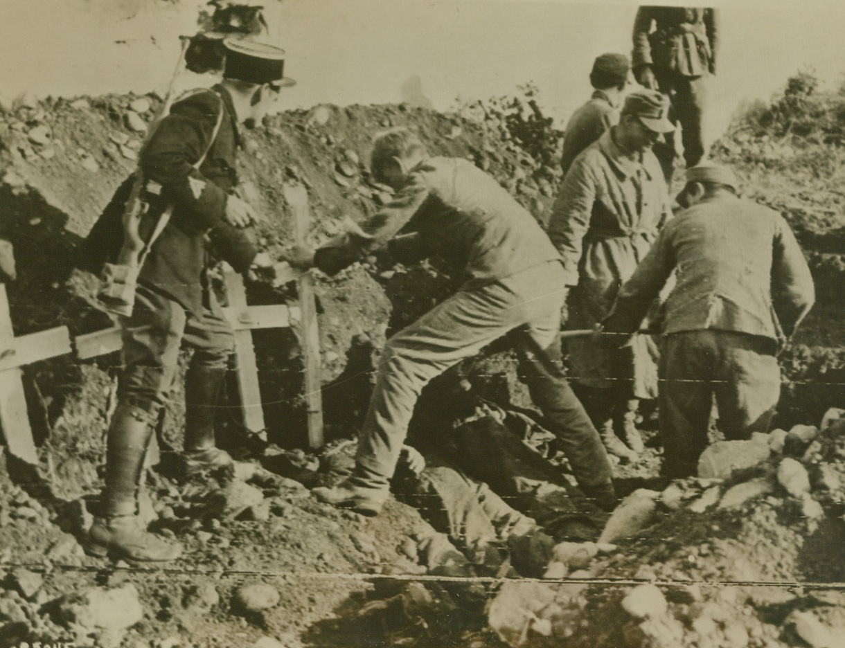 MARKING NAZI GRAVES, 10/2/1944. ELOYES, FRANCE – With the assistance of a French guard, a German prisoner of war plants a marker above the grave of one of his countrymen. At right, other captives shovel earth over the closely packed bodies of Nazi soldiers in this cemetery at Eloyes.Credit: Signal Corps radio telephoto from Acme;