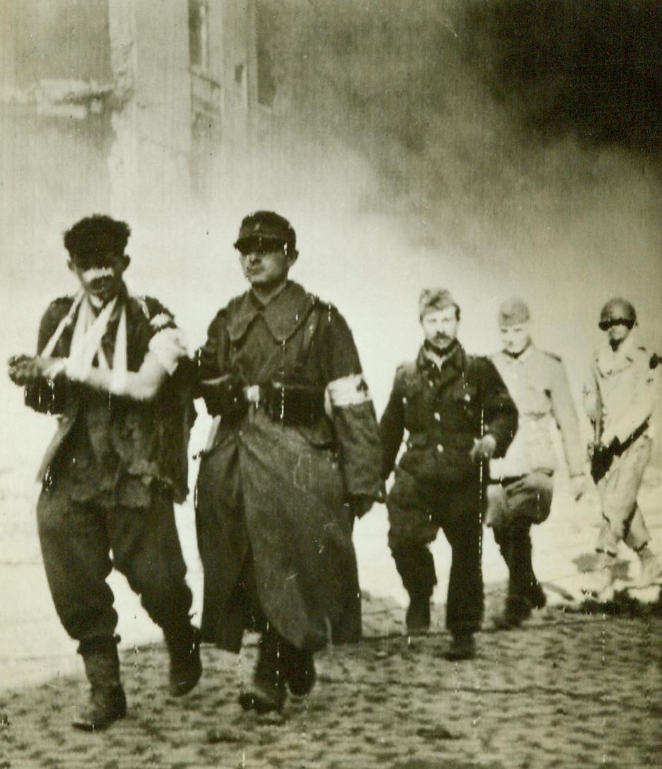 Aachen Defenders, 10/16/1944. Aachen, Germany – German prisoners, some of them wounded, march from the fighting area of Aachen, under the guard of United States soldiers. One of the captives wears the armband of the Medical Corps. 10/16/44 (ACME); Aachen, Germany – German prisoners, some of them wounded, march from the fighting area of Aachen, under the guard of United States soldiers. One of the captives wears the armband of the Medical Corps. 10/16/44 (ACME);