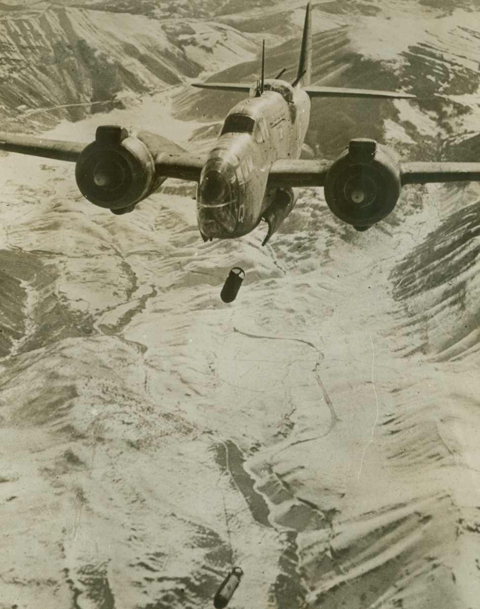 CHIPPING THE ICE OFF NAZI COMUNICATIONS, 2/1/1944. ITALY—An R.A.F. Baltimore lets loose a pair of bombs on the snow-covered town of Sulmona, important Nazi field communications center on the East-West route across Italy. One of the first pictures of R.A.F. support of Allied ground forces on the road to Rome, the photo shows the bomb heading straight for the rail junction and station nestled in the frozen valley. Credit: Acme;