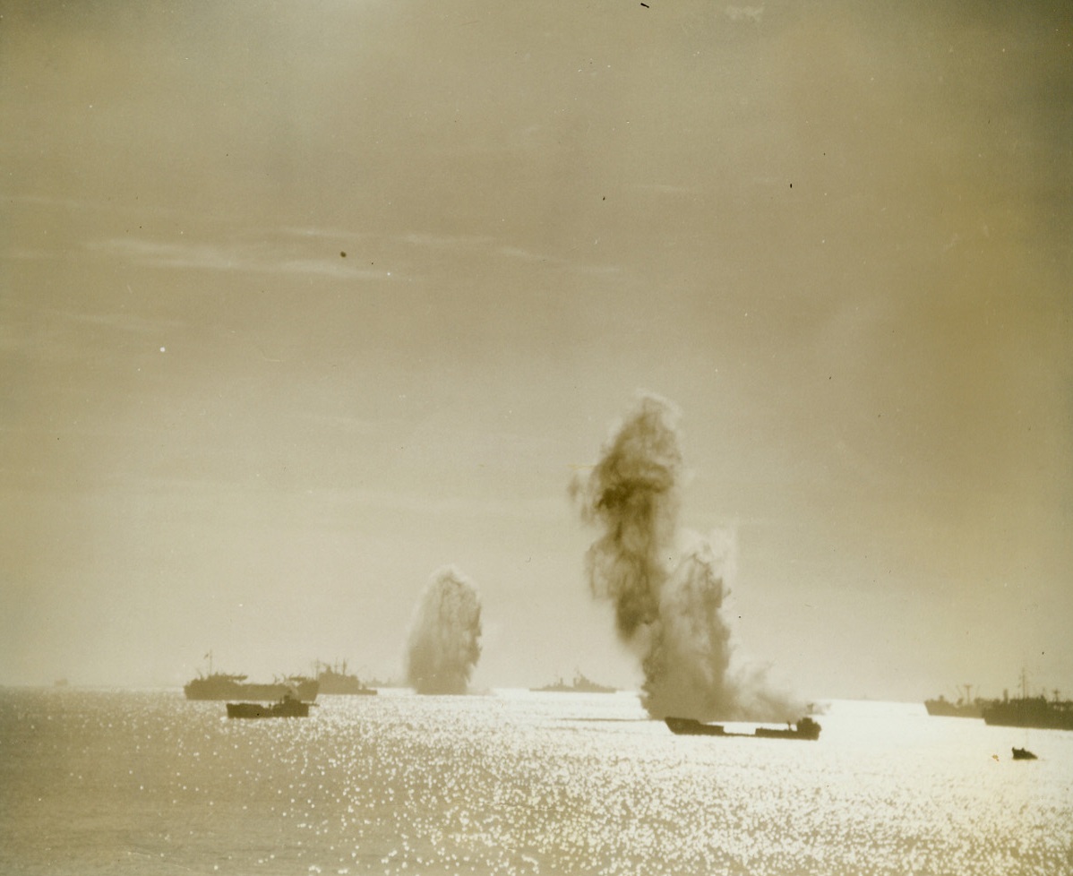 MISSED!—THEY ALWAYS DO, 2/13/1944. ANZIO HORBOR, ITALY—Smoke and water cascade skyward as bombs dropped by Nazi raiders fail to hit their target, landing on the harbor bed. The Germans have tried to bomb these supply ships resting in the harbor at Anzio many times—but they’ve seldom hit the vessels. Credit: Acme photo by Bert Brandt for the War Picture Pool;