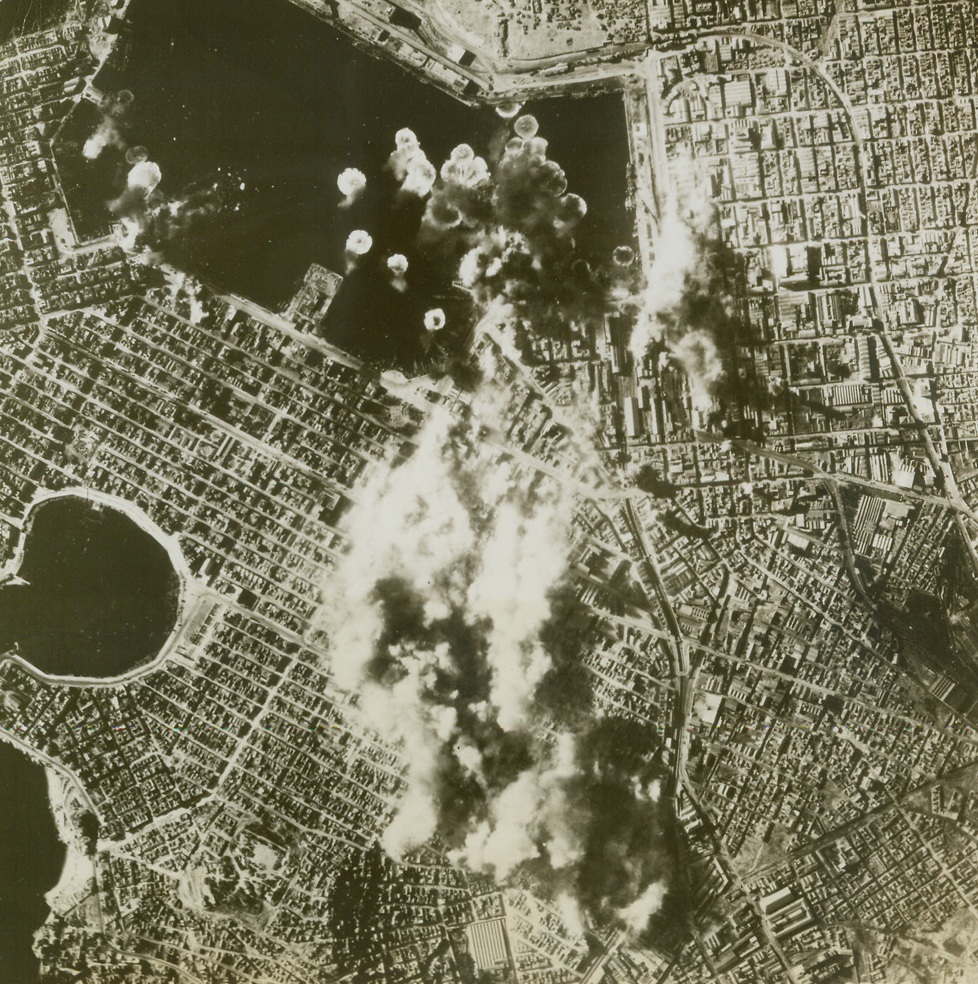 Bomb Athens Harbor, 3/31/1944. ATHENS, GREECE—Clouds of smoke rise from the bomb-battered dock area of Athens, one of the vital German supply centers in the Eastern Mediterranean, after a raid by B-17’s of the U.S. 15th Air Force. German-held airfields near Athens are often the target of raiding American bombers, whose “eggs” are aimed at knocking out Nazi communications in war-torn Greece.  Credit:  U.S. ARMY AIR FORCES PHOTO from ACME.;