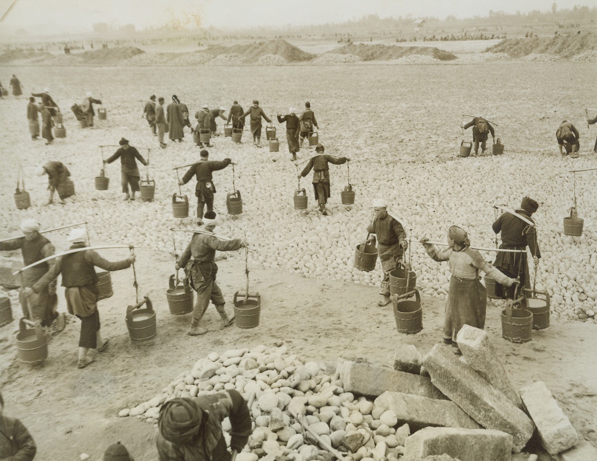 Airfield-Handmade, 3/31/1944. China – Lack of modern equipment and machinery isn’t stopping the resourceful Chinese from building modern airfields in China. Three hundred thousand Chinese workers have been conscripted to do the job. A hundred thousand little handmade wheelbarrows are used to transport materials – and even the chipping of stones for the runways is done by hand. American Engineers, working in conjunction with Chinese Army Engineers, are supervising the job. Photo shows: The Chinese workers pour “slurry” to fill in the holes on a runway. Credit: ACME photo by Frank Cancellare for the War Picture Pool;