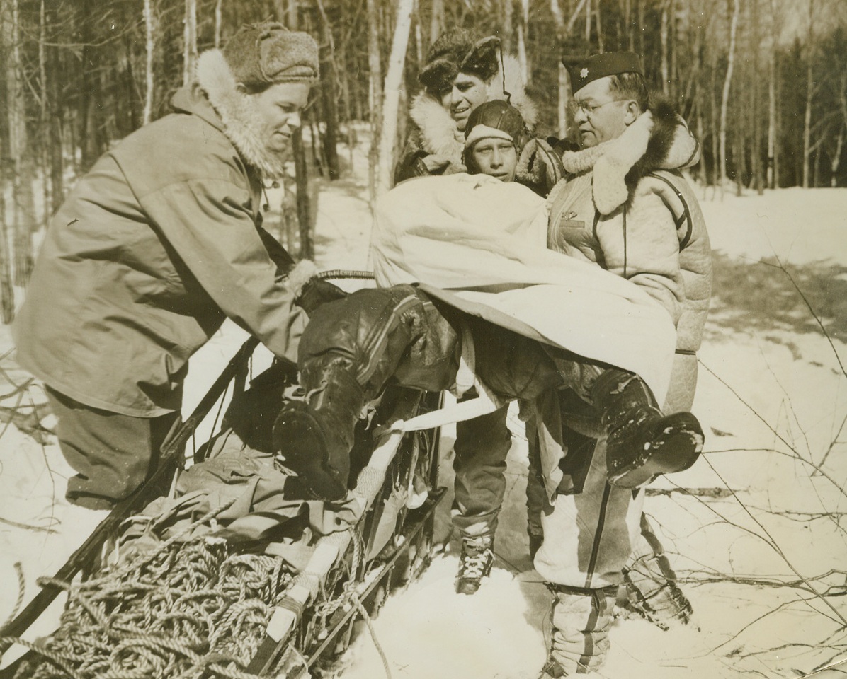 Rescuing Crashed Fliers in the North, 3/7/1944. Manchester, New Hampshire -- To rescue pilots and crewmen of planes forced down in arctic or semi-arctic country, the Search and Rescue section of the North Atlantic Wing of the Air Transport Command has been organized. Equipped and trained to cover difficult terrain in all kinds of weather, the base camps of the section are always ready to answer call for assistance. This series of photos taken at a Search and Rescue section base camp at Manchester shows how a crashed flier is rescued. While this was not an actual case of answering a distress call, the instance was carefully staged to follow the procedure of a typical rescue.  New York Bureau After the “injured” pilot has received first aid, he is placed on the sled for the trip back to the base. Left to right, Sgt. Charles Clifton, Maj. Norman D. Vaughan, and Maj. Daniel Maunz. The man playing the role of the injured pilot was not identified. Credit: ACM;