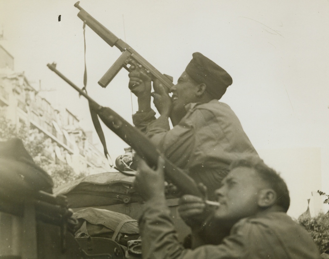 SNIPE AT NAZI SNIPERS IN PARIS, 3/30/1944. FRANCE – Two members of the French armored division, one with a cigarette in his mouth, fire at snipers in a Paris building as they cover the entry of the main column of French troops into the French capital. Credit: Acme photo by Charles Haacker, War pool correspondent;